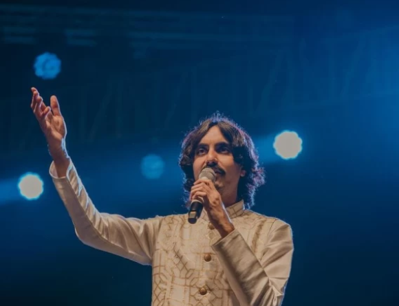 Aditya Gadhvi performing live on stage during a Navratri Garba night, a large crowd dancing in traditional outfits.