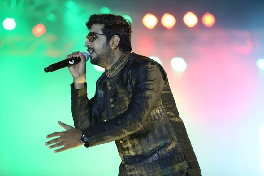 Jigardan Gadhavi performing live on stage during a Navratri Garba night, a large crowd dancing in traditional Gujarati outfits.