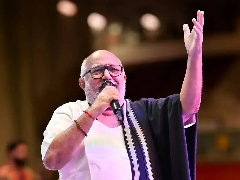 Atul Purohit performing live in his signature white kurta and black shawl during a Garba night, a large crowd dancing in traditional outfits.